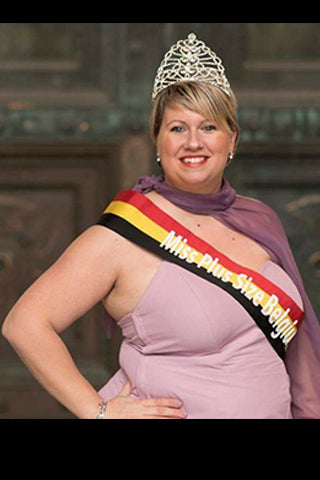 Une femme couronnée souriante porte une écharpe "Miss Plus Size Belgium" et une élégante robe violette.