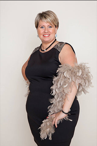 Une femme souriante pose en robe noire élégante, ornée d’un boa en plumes beige.